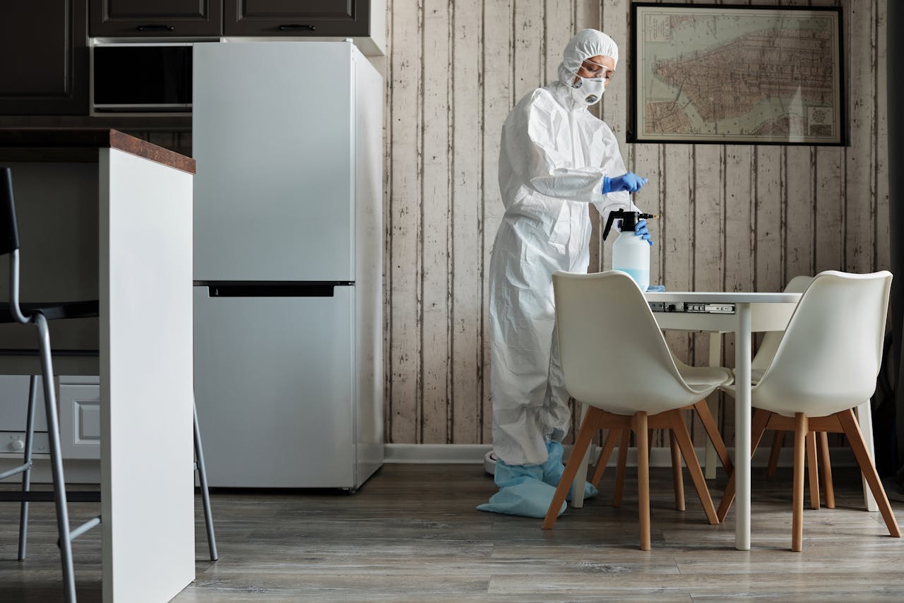 get-in-touch Person in hazmat suit disinfecting a modern kitchen table with spray bottle for hygiene.