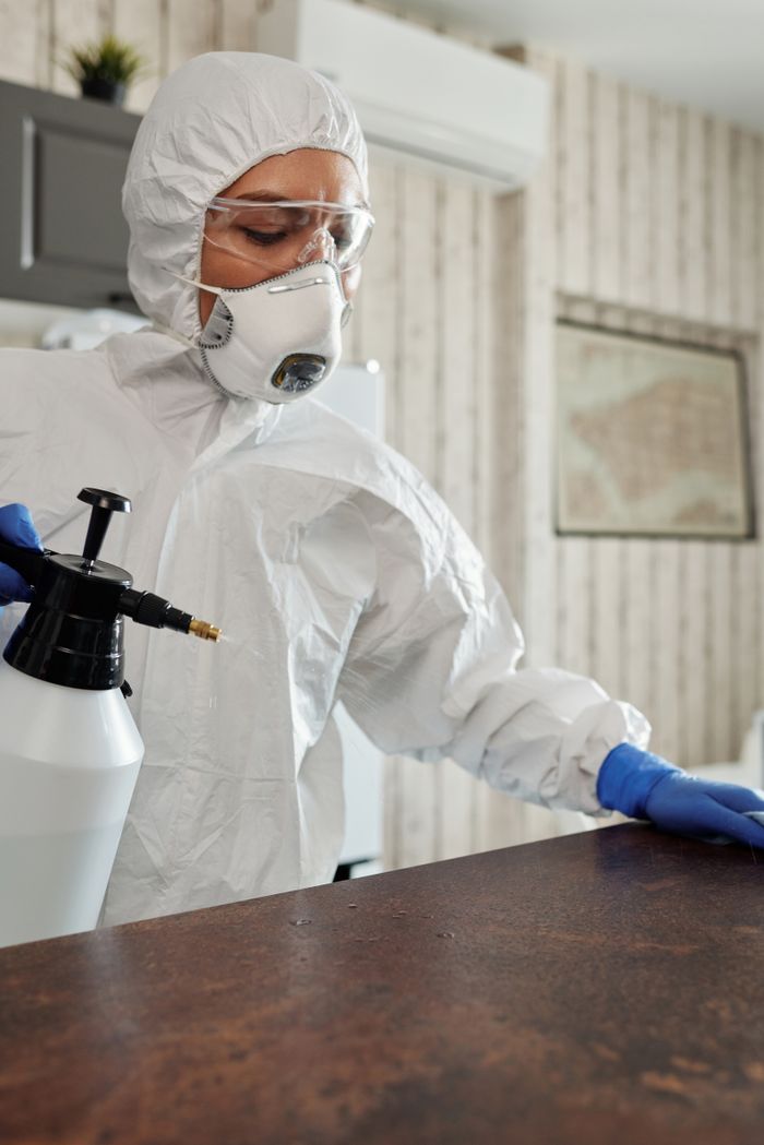 services-02 Person in protective suit disinfecting indoor surfaces with spray.